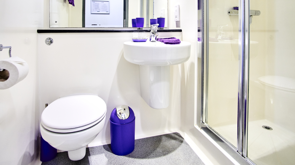 A bathroom with a toilet, sink and partial shower view